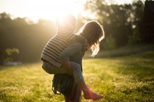 Image of a Mother Carrying Her Son on Her Back in an Open Field at Sunset, Illustrating the Concept of Godparents and Guardians in Young Family Estate Planning